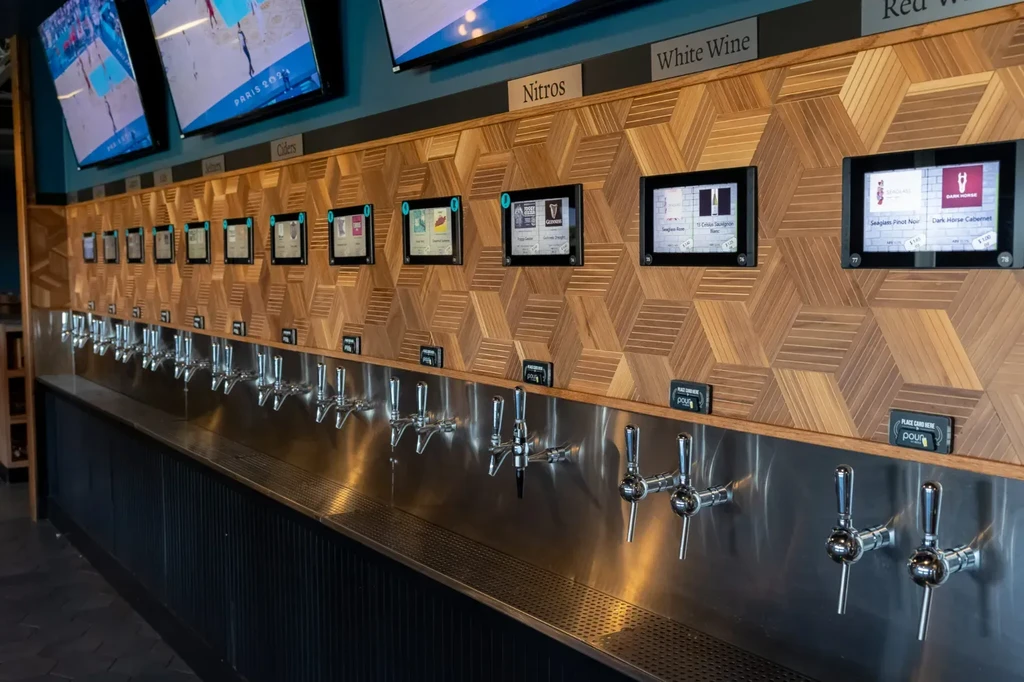 Modern self-pour beverage wall with taps and digital info screens.
