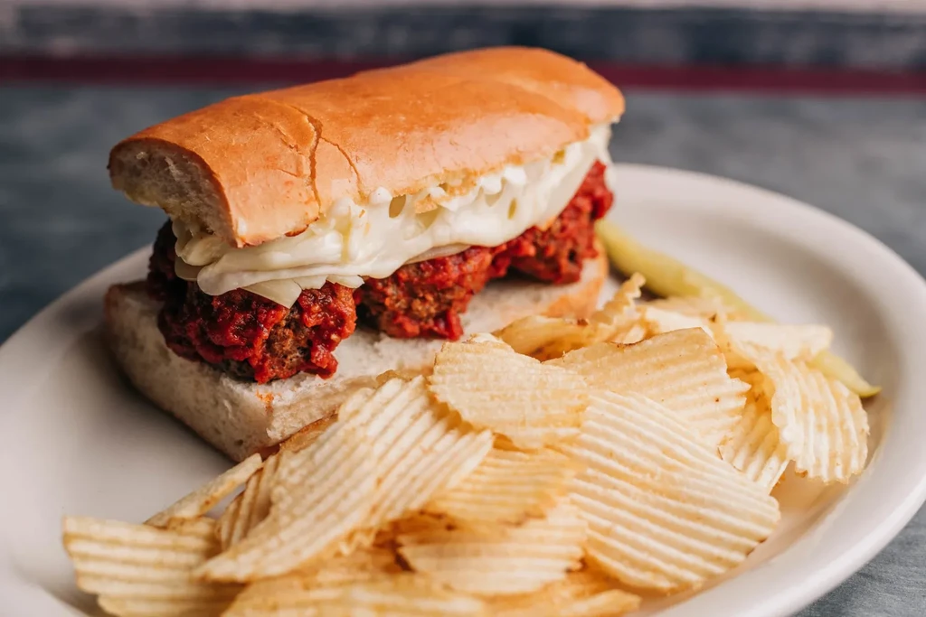 Meatball sub, melted cheese, ridged potato chips, and a pickle spear.