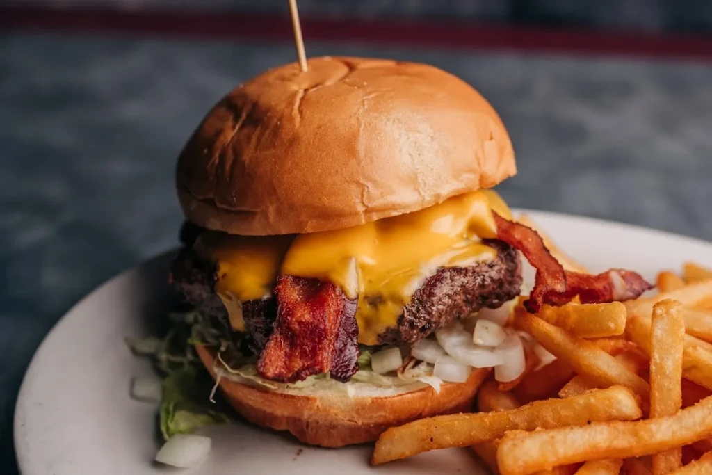 Cheeseburger with bacon, melted cheese, lettuce, onions, and fries on plate.