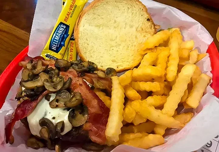 Deconstructed burger, fries, and mayonnaise packet in a red basket.