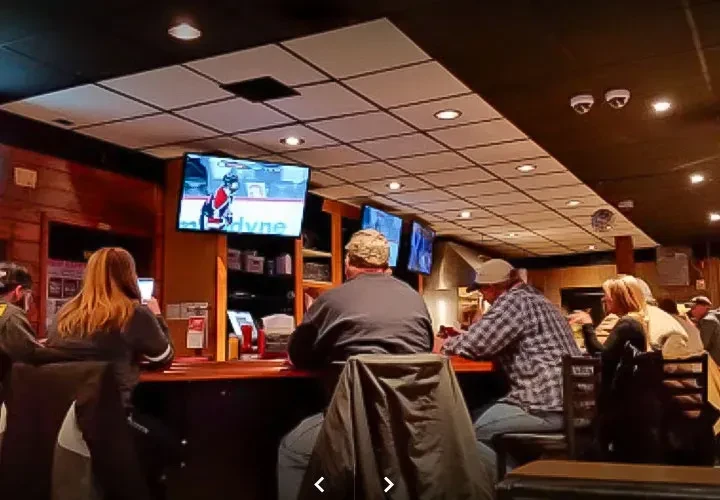 Dark sports bar interior with patrons watching hockey on screens.