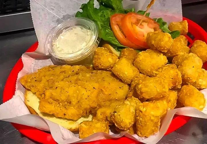 Crispy fried sandwich, tater tots, lettuce, tomato, and sauce in basket.