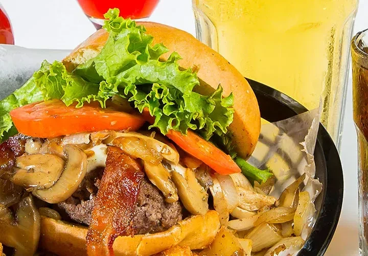 Gourmet burger with lettuce, tomato, bacon, mushrooms, and fries.