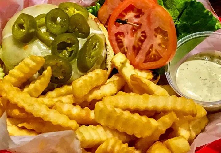 Jalapeño cheeseburger, crinkle fries, tomatoes, and green dip in a red basket.