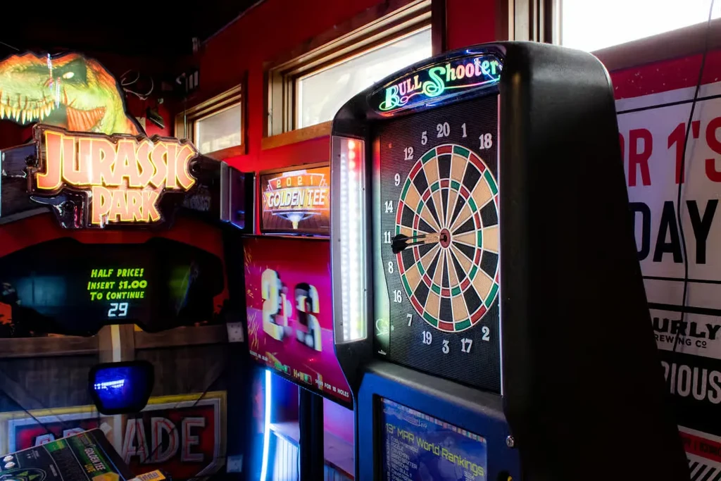 Brightly lit arcade games in a bar: Bull Shooter, Golden Tee, Jurassic Park.