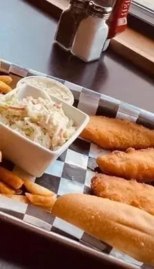 Fried fish, fries, coleslaw, and roll on a checkered tray.