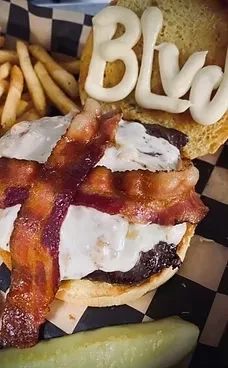 Open-faced burger with bacon, melted cheese, fries, and 'BLVD' on bun.