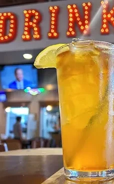 Glass of iced drink with lemon, 'DRINK' sign in blurred background.