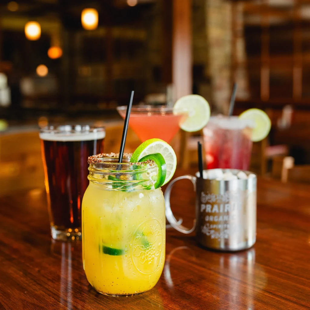 Four different alcoholic drinks, including a jalapeño cocktail, on a wooden table.