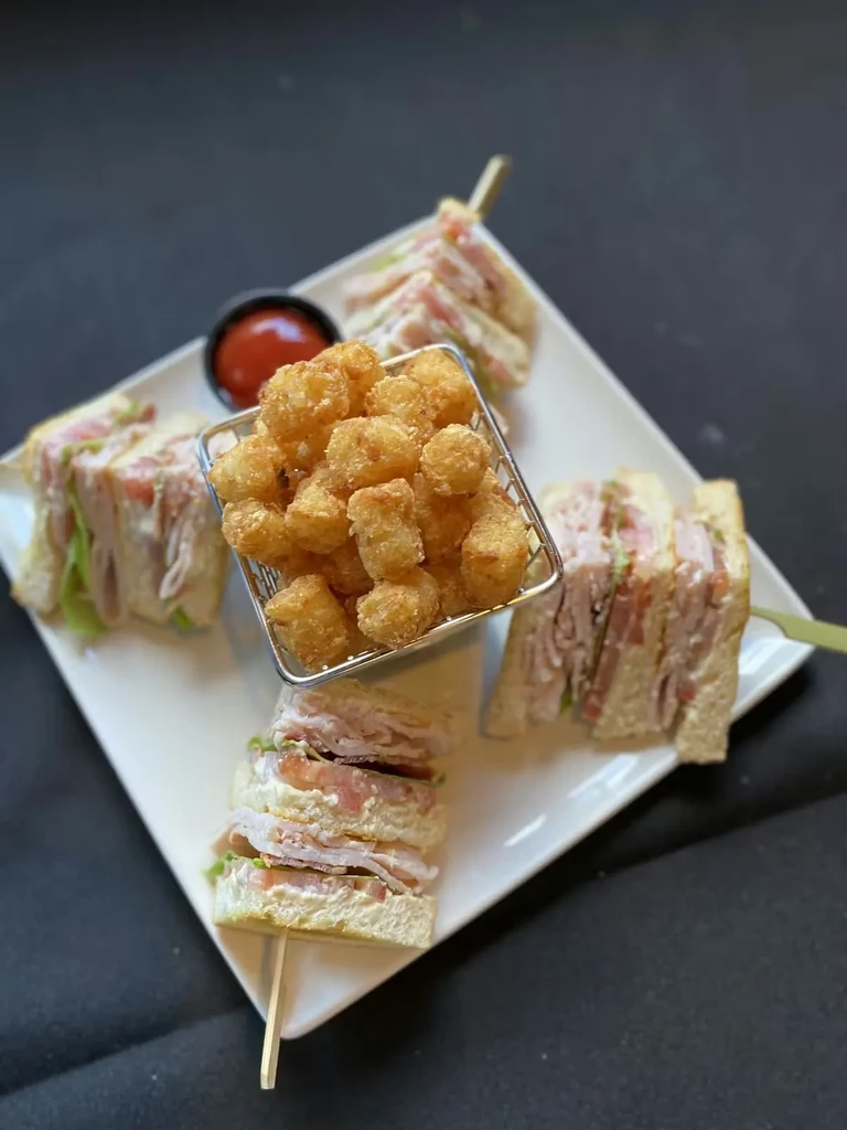Club sandwiches, tater tots, and red sauce on a white plate.