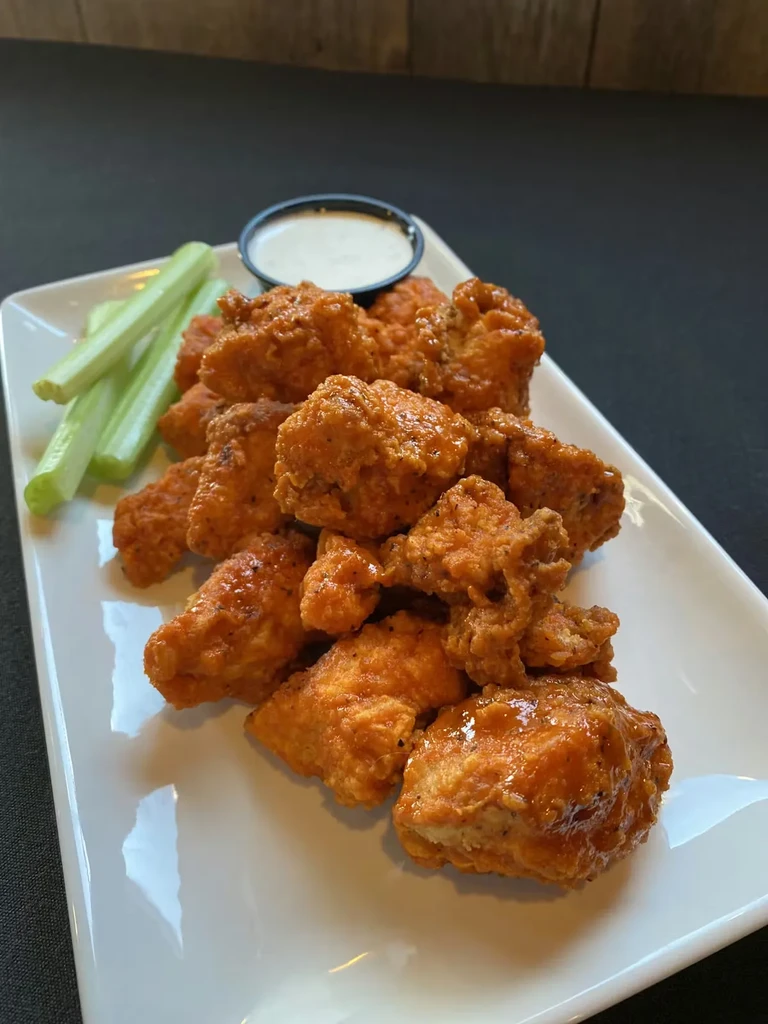 Sauced boneless chicken wings, celery, and white dip on a plate.