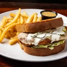Hearty breaded sandwich, crispy fries, and dipping sauce on a plate.