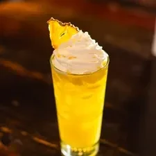 Vibrant yellow frothy drink with whipped cream and pineapple slice.