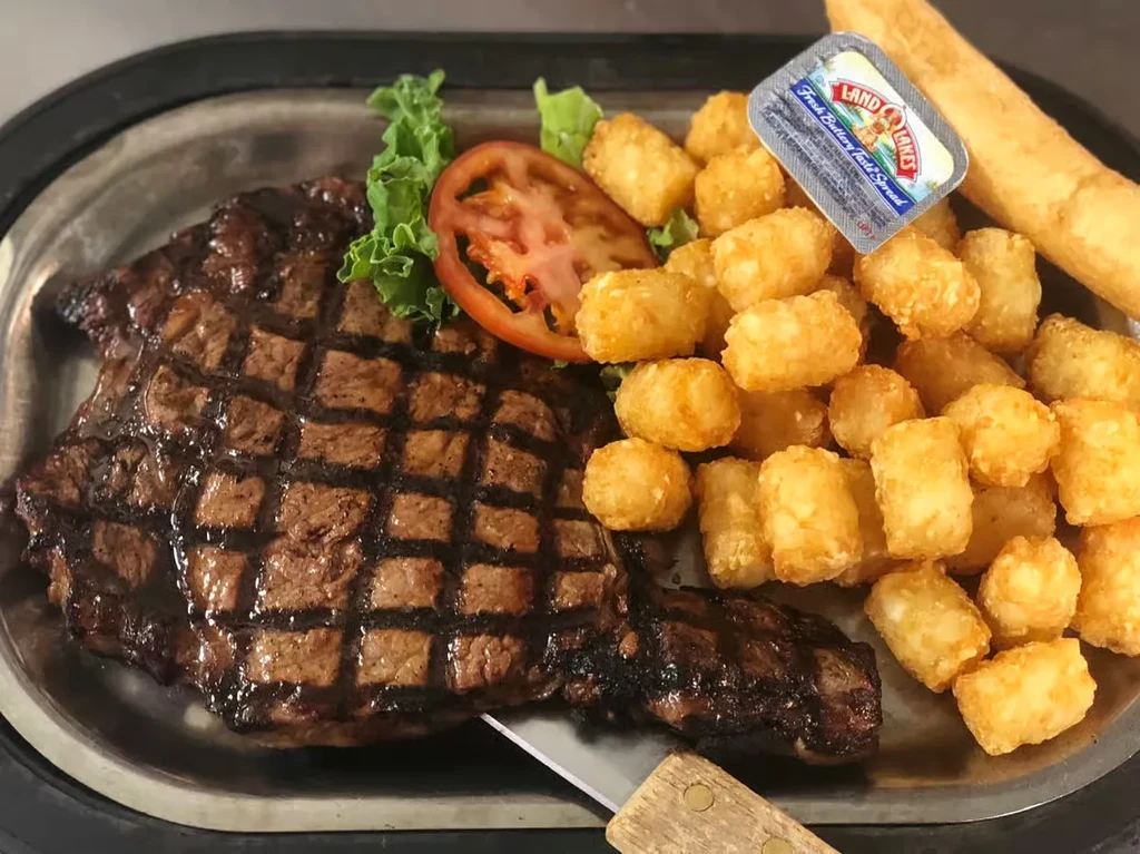 Overhead: grilled steak, tater tots, tomato, lettuce, and butter packet.