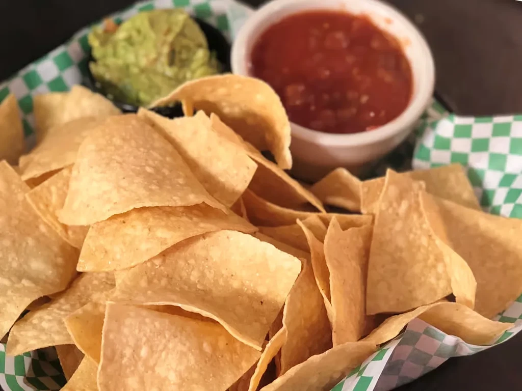 Basket of golden-brown tortilla chips with guacamole and salsa.