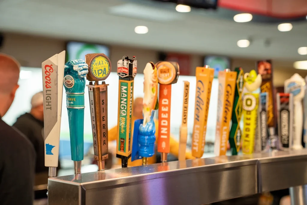 Ten diverse beer tap handles with unique branding on a bar.