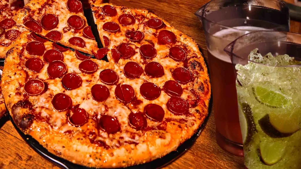 Partially sliced pepperoni pizza, green lime drink, and amber drink.