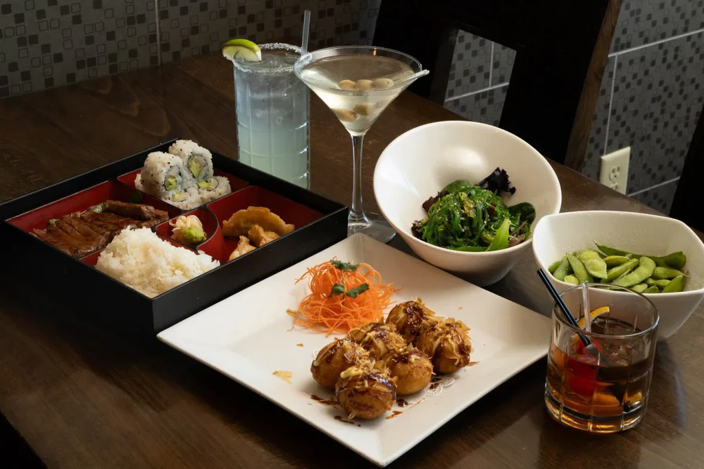 Japanese food spread with takoyaki, bento box, salads, and cocktails.
