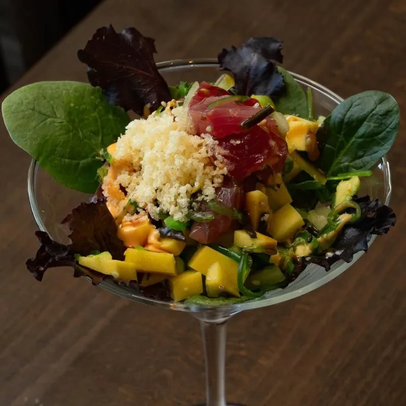 Layered poke salad with tuna, mango, crispy topping in martini glass.