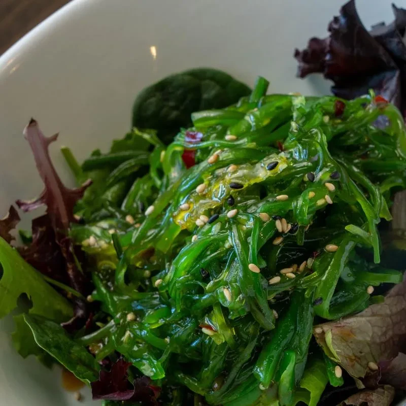 Vibrant green seaweed salad with sesame seeds and dressing in white bowl.