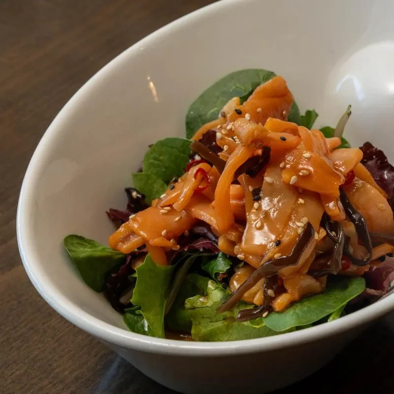 Salad with leafy greens, orange seafood, seaweed, chili flakes, sesame seeds.