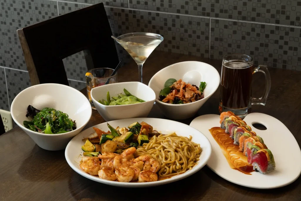 Assorted Japanese dishes: shrimp noodles, sushi, salads, and various drinks.