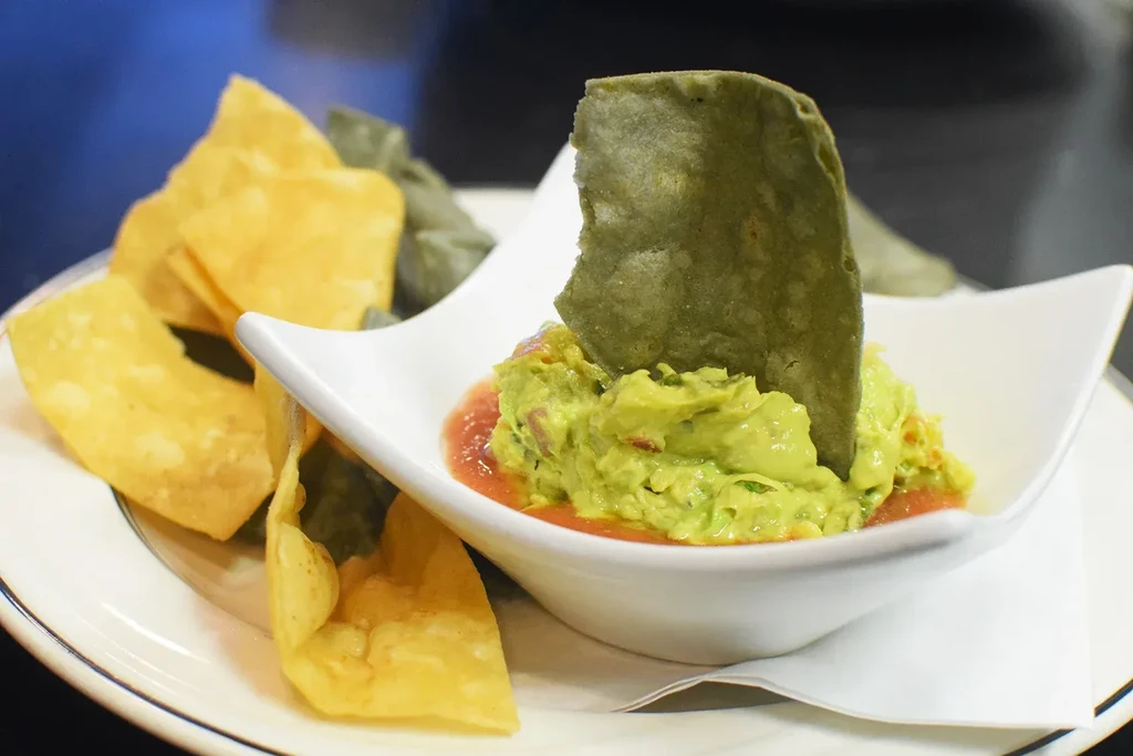 Vibrant guacamole and salsa served with golden and dark green chips.
