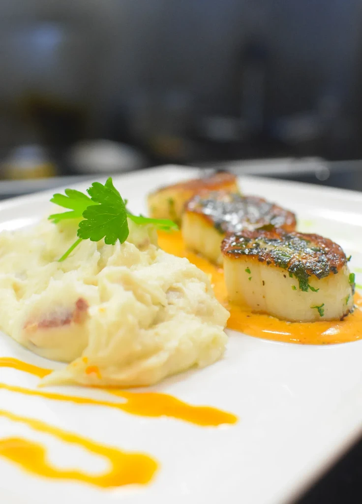 Three seared scallops, mashed potatoes, and orange sauce.