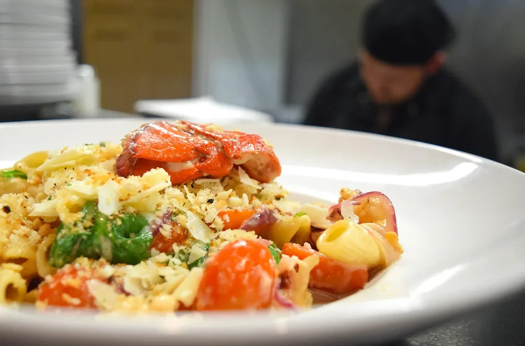Close-up of plated lobster pasta with cheese, vegetables, and breadcrumbs.