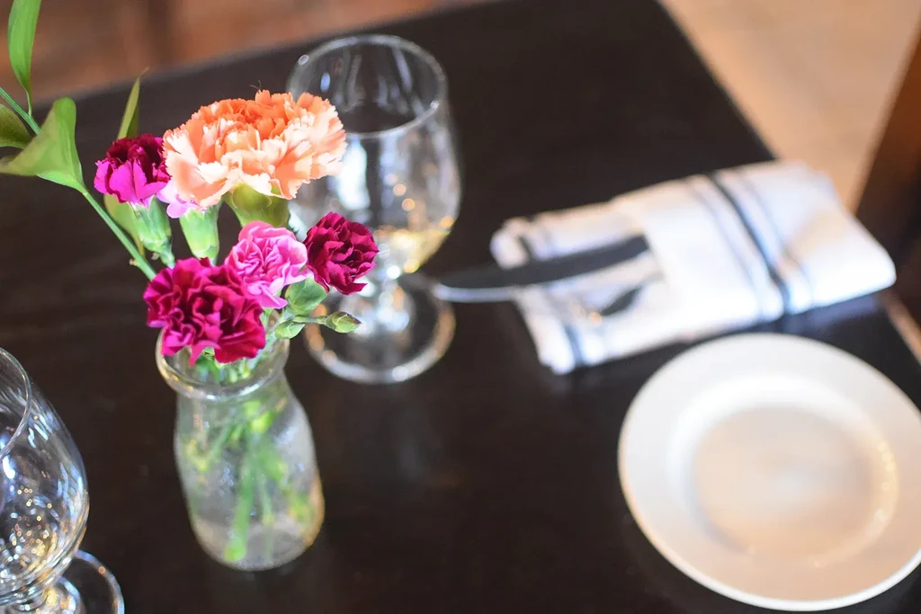 Fuchsia, pink, orange carnations in vase on dark dining table.