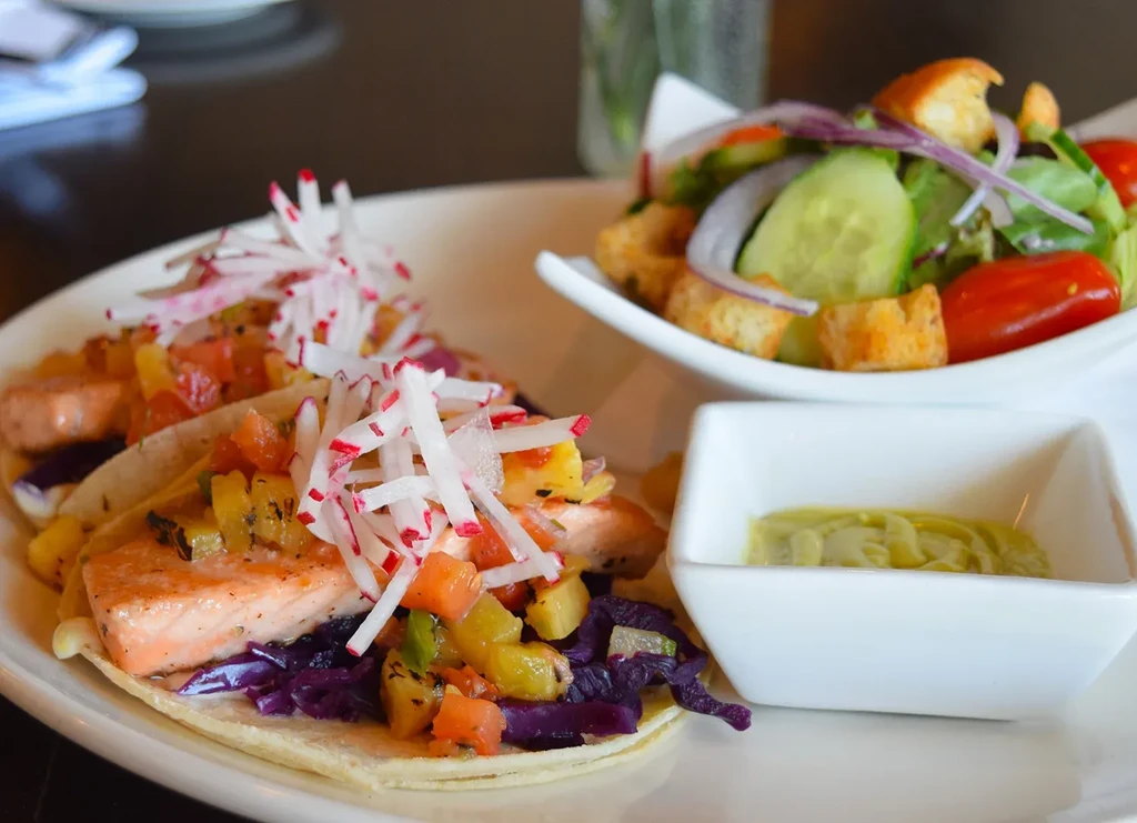 Two salmon tacos with mango salsa, radishes, green sauce, and salad.
