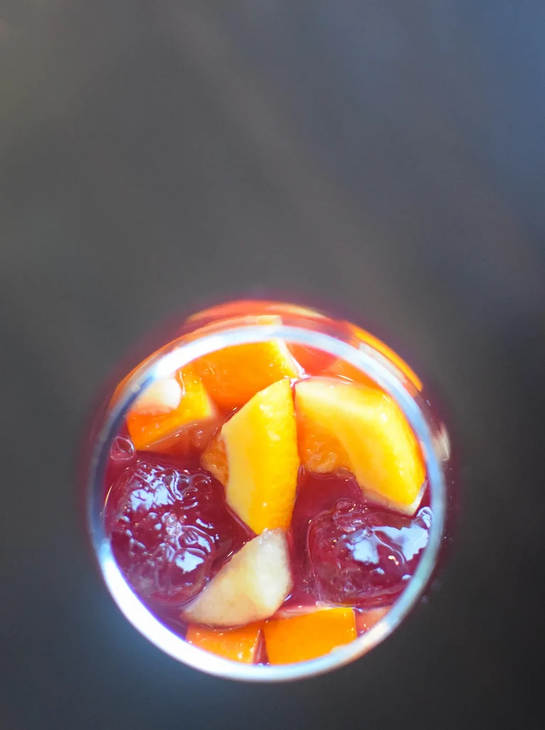 Colorful fruit punch in a glass with orange, yellow, and red fruits.