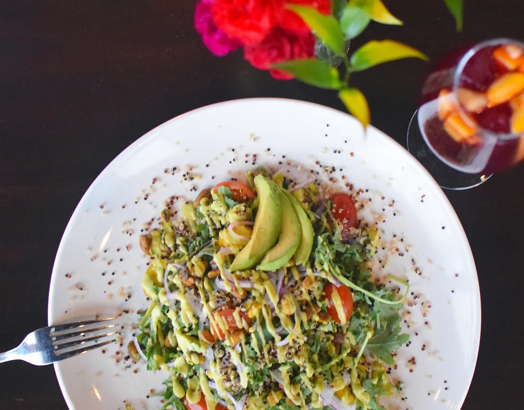 Overhead colorful salad on white plate with avocado, tomatoes, nuts.