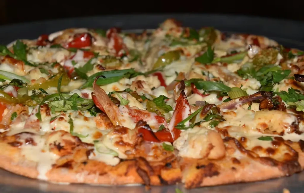 Close-up of freshly baked pizza with chicken, cheese, vegetables, and sauce.