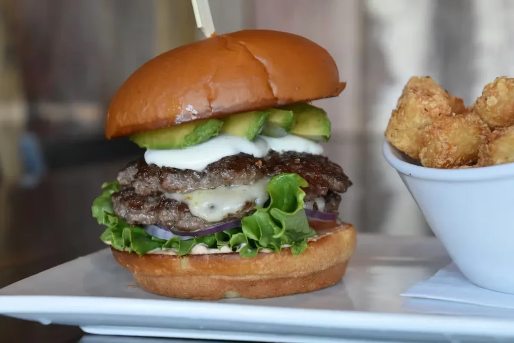 Tall double-patty burger with avocado and crispy potato bites.