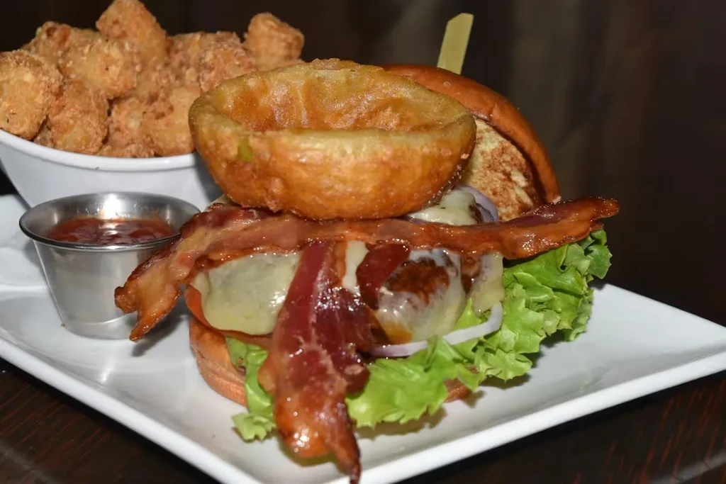 Stacked gourmet burger, onion ring, tater tots, and dipping sauce.