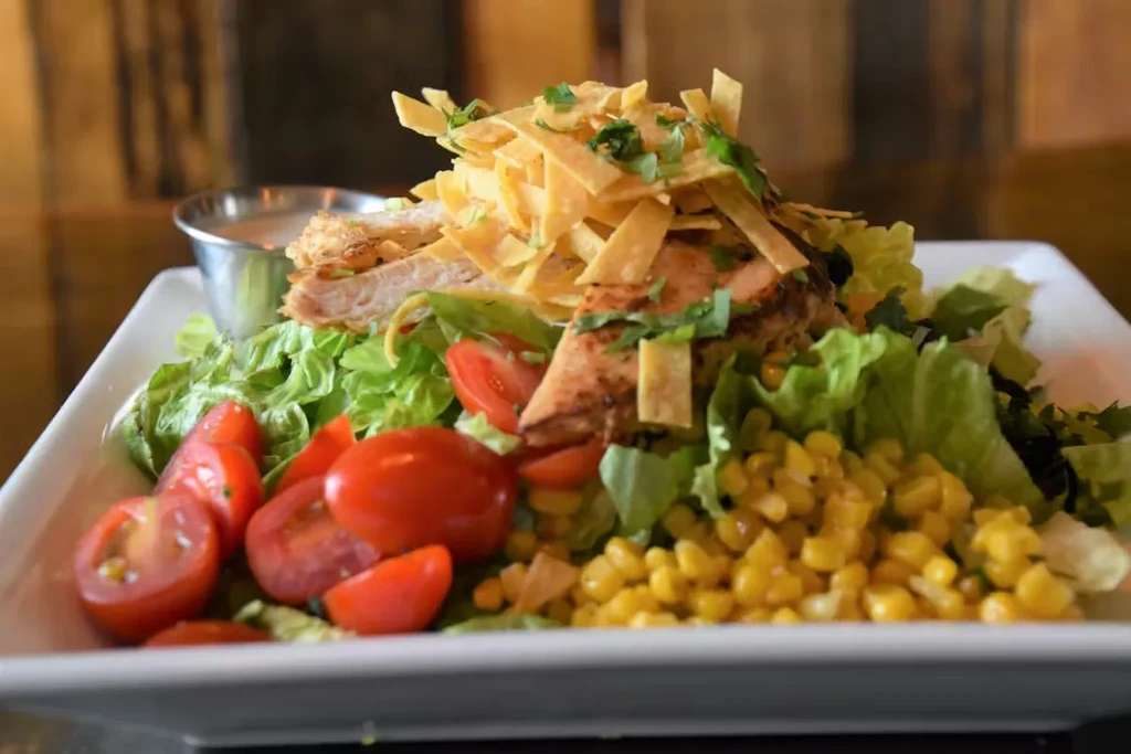 Colorful grilled chicken salad with lettuce, tomatoes, corn, and tortilla strips.