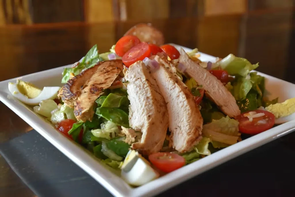 Grilled chicken salad with lettuce, tomatoes, and egg on a plate.