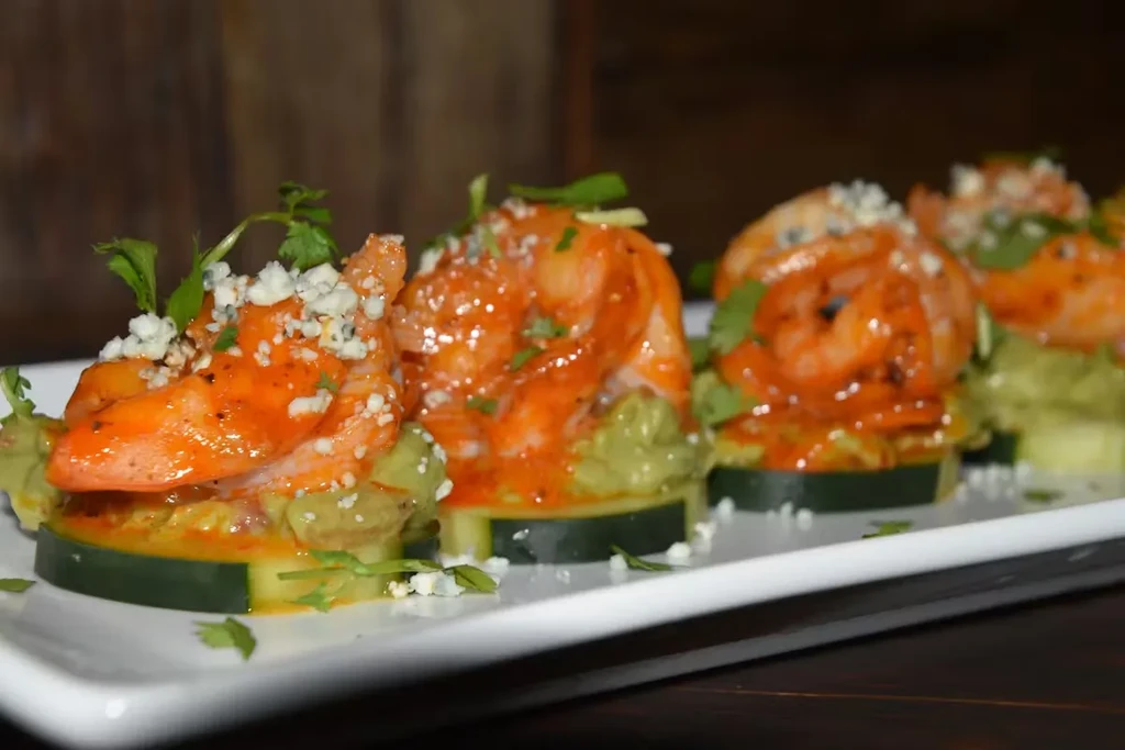 Close-up of shrimp, avocado, and cucumber appetizers on a white plate.