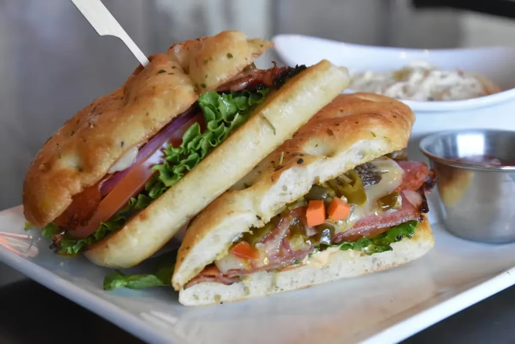 Focaccia sandwich halved, revealing meats, cheese, lettuce, tomato, and pickles.