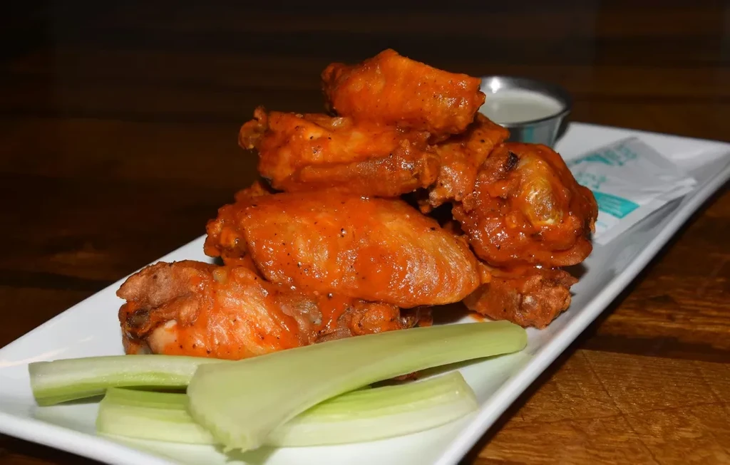 Rectangular plate of buffalo wings, celery, and white dipping sauce.