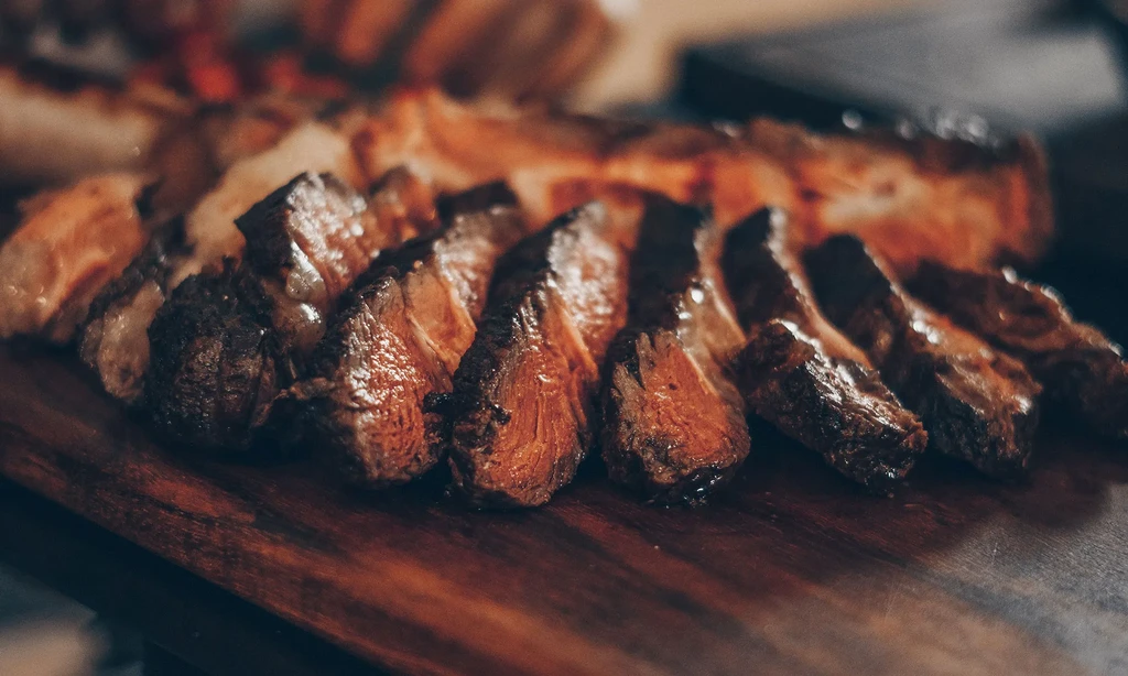 Thickly sliced seared medium-rare steak on a dark wooden board.