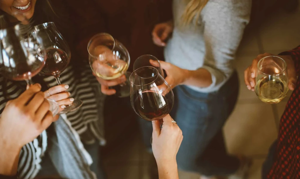 Multiple hands holding wine glasses with red and white wine.