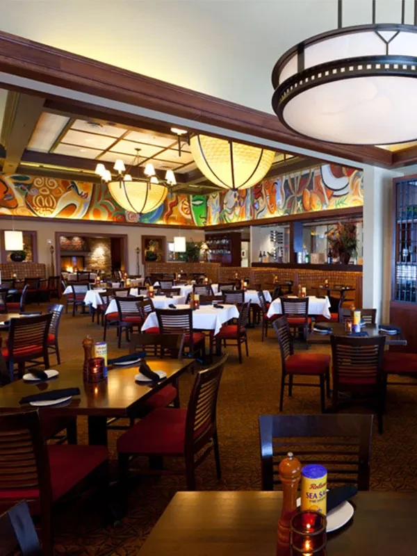 Empty, spacious restaurant dining room with colorful mural and warm lighting.