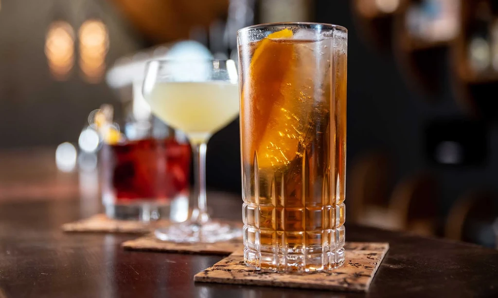 Three cocktails on a dark wooden bar, one garnished with orange peel.