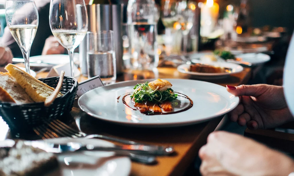 Diner's hands holding an elegant salmon dish with champagne.
