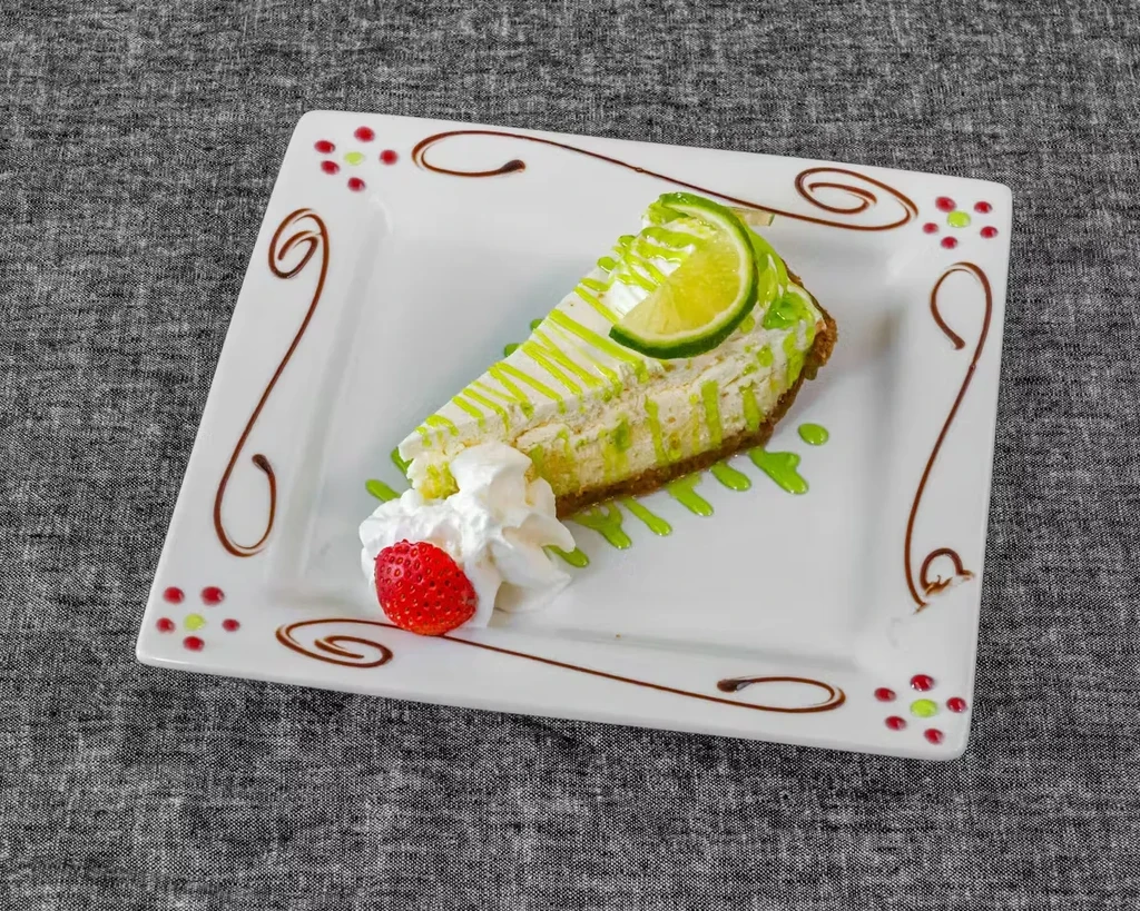 Key lime pie slice with lime, whipped cream, and strawberry.