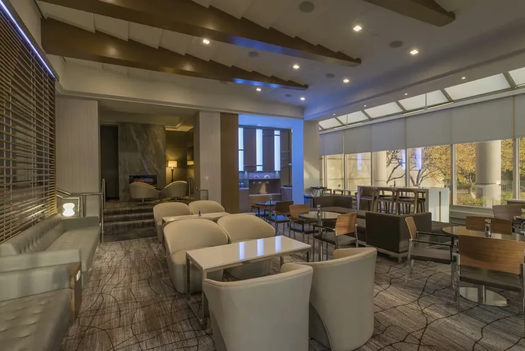 THOUGHT
The user wants a short, factual alt-text (7-12 words) based on the image description.
It needs to be concise and descriptive, with no marketing language.
I need to summarize the key visual elements: a modern, spacious lounge/restaurant with various