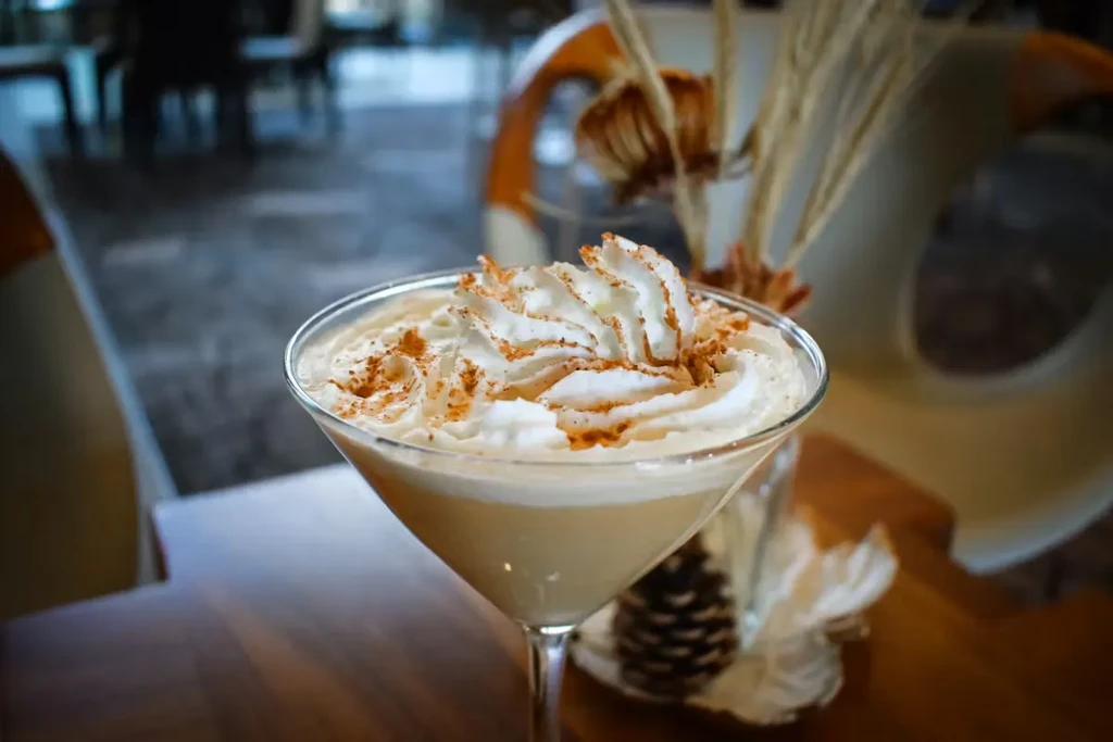 Creamy drink in martini glass topped with whipped cream, cinnamon, pinecone.