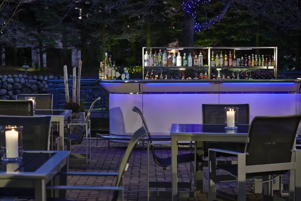 Outdoor bar with glowing purple-blue front and candlelit dining tables.